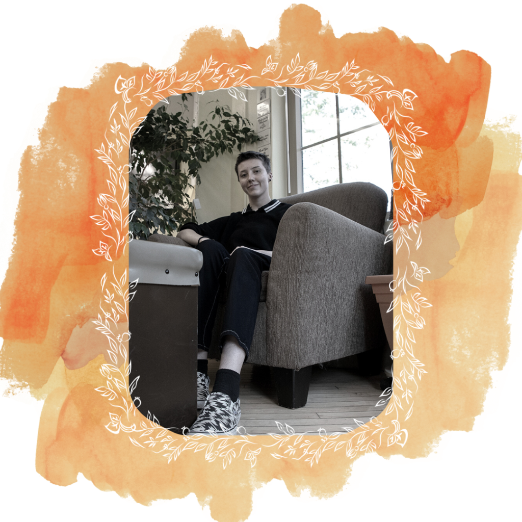 A photo of Abbie Steuhm sitting in a chair. The photo is framed by orange watercolor paint and white leaves.